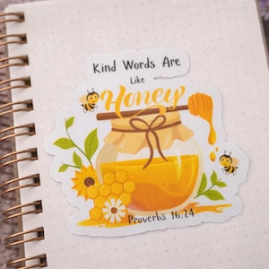 May include: A sticker with a honey theme, featuring a jar of honey, a honey dipper, and two bees. The text "Kind Words Are Like Honey" and "Proverbs 16:24" are also included. The sticker is on a dotted notebook.