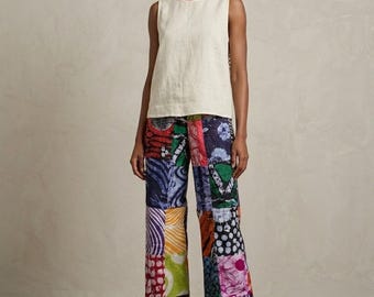 Puede incluir: Una blusa sin mangas de color crema combinada con pantalones anchos con un diseño de patchwork multicolor. Los pantalones muestran varios patrones, incluyendo rayas, círculos y formas orgánicas en tonos rojos, azules, verdes y amarillos, con zapatillas blancas.