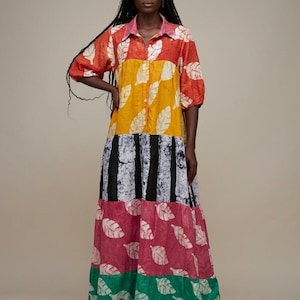 May include: A long, button-down dress featuring a tiered design with various patterns and colors. The top section is orange with white leaf prints, the middle is yellow with white leaf prints, the next is black and white stripes, and the bottom is pink and green with white leaf prints.