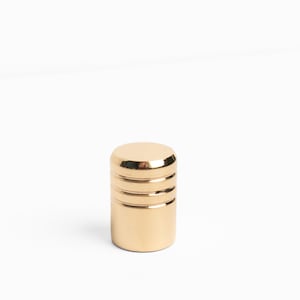 May include: A gold metal knob with a cylindrical shape and three horizontal grooves.