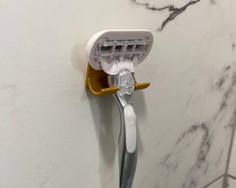 May include: A gold-colored razor holder with a white razor attached to it. The razor has a silver handle and a white head with five blades.