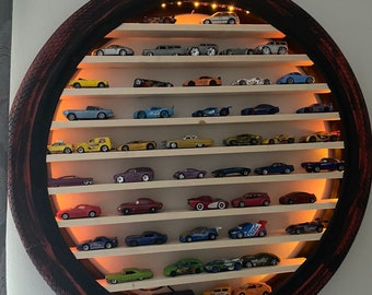 May include: A circular tire-shaped shelf with multiple shelves for displaying toy cars. The shelves are made of wood and the tire is painted black with red accents. The tire has the text "SNAKESKIN 2" printed on it. The shelves are lit with small LED lights.