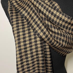May include: A black and tan houndstooth pattern scarf draped over a black mannequin. The scarf is made of a soft, woven material. The pattern is a classic design, with small, repeating squares.