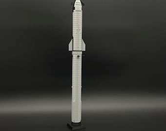 May include: A grey and black model rocket, standing upright on a black base. The rocket has a cylindrical body with detailed paneling and a pointed nose cone. The rocket is a detailed replica of a spacecraft.