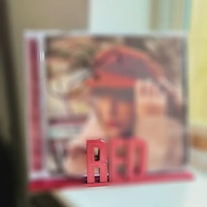 Puede incluir: Una letra "R" de madera roja se encuentra frente a una imagen borrosa. La palabra "RED" está escrita con letras de madera roja. El fondo está desenfocado.