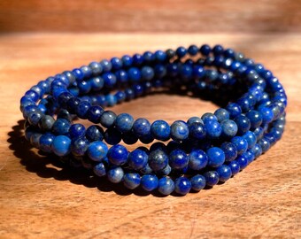 May include: A stack of blue lapis lazuli beaded bracelets. The bracelets are made of small, round beads and are stacked on top of each other.