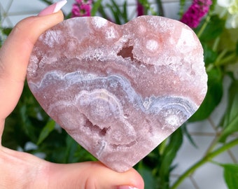 May include: A heart-shaped pink and white agate crystal with a natural, polished finish. The crystal has a swirling pattern of pink and white, and a few small holes.