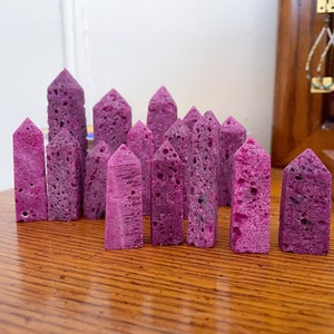 May include: A collection of 15 purple, rough-textured, crystal-shaped stones arranged in a row on a wooden surface.