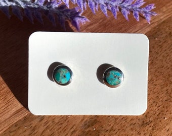 May include: A pair of silver stud earrings with turquoise stones. The earrings are on a white card.