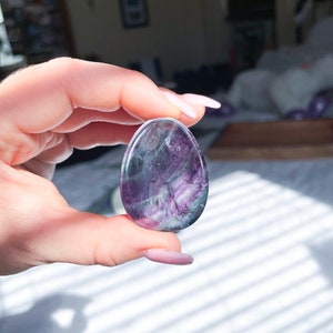 May include: A smooth, oval-shaped fluorite crystal with purple, green, and white swirls. The crystal is polished and has a translucent appearance.