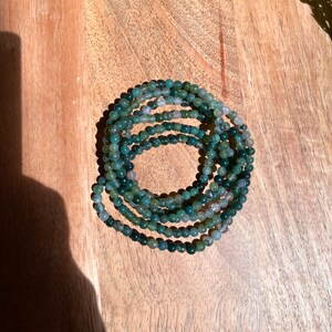 May include: A stack of green and gray agate bead bracelets. The beads are small and round, and the bracelets are stacked on top of each other.