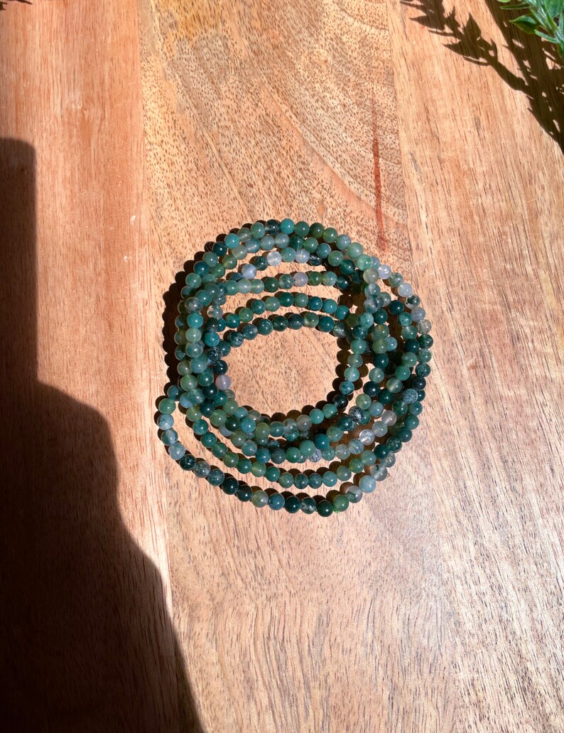May include: A stack of green and gray agate bead bracelets. The beads are small and round, and the bracelets are stacked on top of each other.