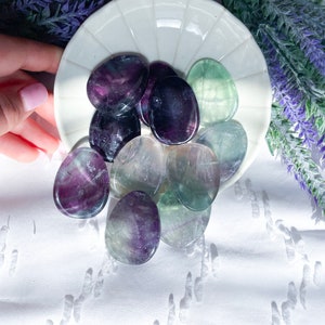 May include: A collection of polished fluorite stones in shades of green, purple, and white. The stones are arranged on a white plate with a scalloped edge.