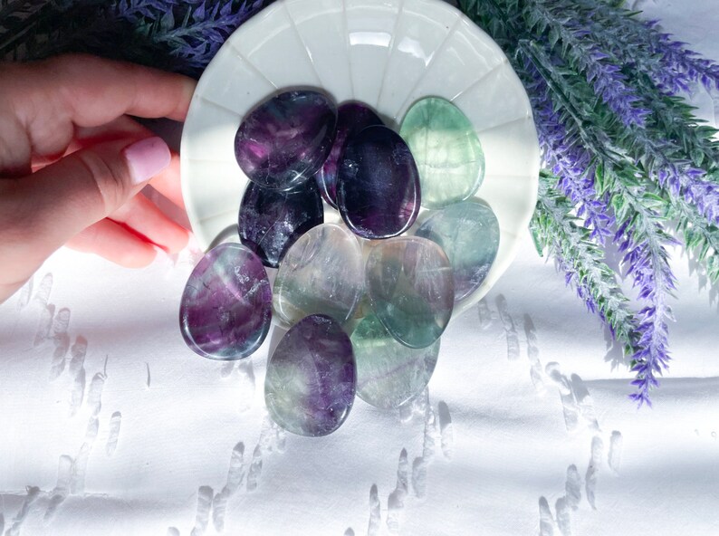 May include: A collection of polished fluorite stones in shades of green, purple, and white. The stones are arranged on a white plate with a scalloped edge.