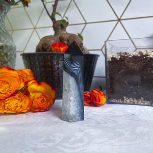 May include: A white ceramic mug with a black handle and the text "But First, Coffee" in a bold, black font. The mug is set against a blurred background, suggesting a cozy setting.