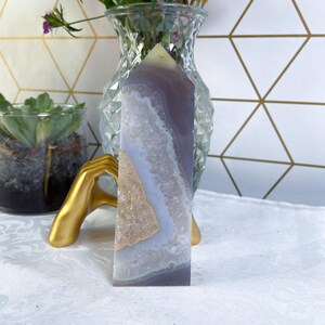 May include: A purple and white agate crystal point with a natural druzy finish. The crystal is polished and has a smooth, glassy surface.