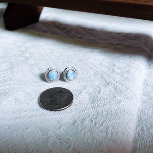 May include: A pair of silver stud earrings featuring a round blue gemstone set in a halo of small clear stones.