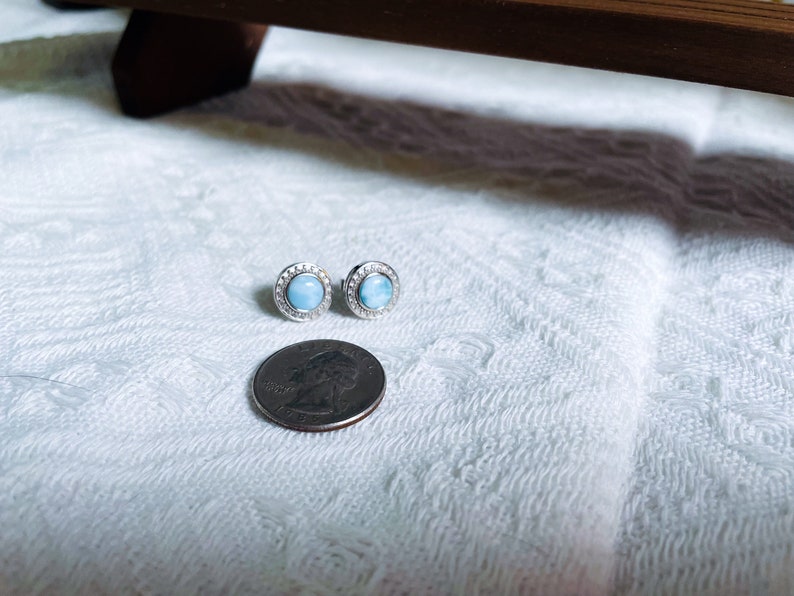May include: A pair of silver stud earrings featuring a round blue gemstone set in a halo of small clear stones.