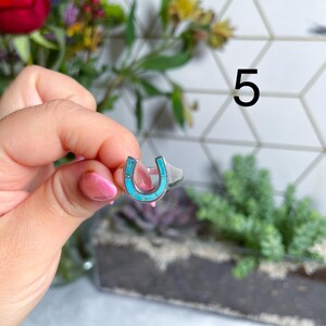 May include: A silver ring with a turquoise horseshoe design. The ring is on a finger.