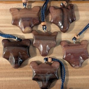 May include: Six wooden wolf head pendants with dark brown and purple wood grain. Each pendant is attached to a dark blue cord with wooden beads.