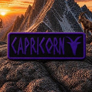 May include: A rectangular patch with the word "KAPRIKORN" in purple, stylized lettering. The patch has a black background and a purple border. The image features a mountain landscape with goats and a sunset.
