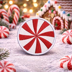 May include: A circular patch featuring a red and white peppermint candy design, edged with white. The image includes other peppermint sweets, candy canes, and a gingerbread house, set against a snowy backdrop. Christmas theme.