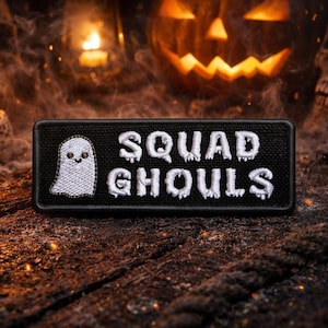 Peut inclure: Écusson rectangulaire noir avec le texte brodé blanc « SQUAD GHOULS » et un motif de fantôme. L'écusson est placé sur un fond sur le thème d'Halloween avec une citrouille sculptée, un crâne et des bougies.