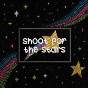 May include: Embroidered patch with the text "shoot for the stars" in white. The patch features a gold star and a colorful rainbow trail against a black background. Additional gold and white stars are scattered around the patch.