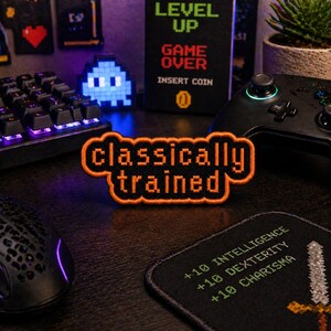 May include: A collection of gaming accessories, including a black keyboard, mouse, and controller. A patch with the words "classically trained" in orange and black is in the center. Other items include a "Level Up" sign and a pixelated blue ghost.
