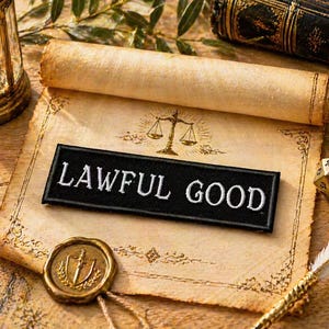 May include: A black patch with white embroidered text reading "LAWFUL GOOD" rests on a parchment. The parchment has a gold seal and a rolled scroll. A gold scale of justice is above the patch. A candle lantern, a book, and a 20-sided die are also visible.