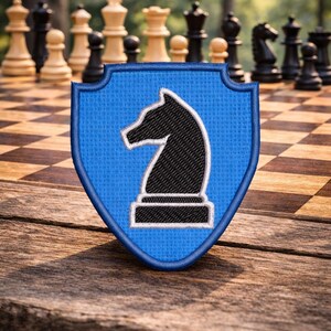 May include: A blue shield-shaped patch with a black chess knight design and a white outline. The patch is set against a blurred background of a chessboard and chess pieces, resting on a wooden surface.