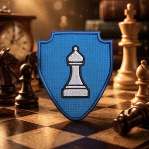 May include: A blue shield-shaped patch featuring a white and black bishop chess piece. The patch is on a chessboard with other chess pieces in the background, including a king, knight, and pawn. A clock and books are also visible.
