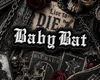 May include: A black and white embroidered patch with the words "Baby Bat" in gothic lettering. The patch is surrounded by gothic-themed items, including a skull, roses, and chains.