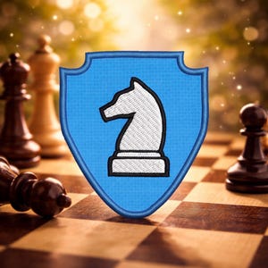 May include: A blue shield-shaped patch with a white chess knight design and black outline. The patch is on a wooden chessboard with chess pieces in the background. The knight is a prominent symbol in chess.