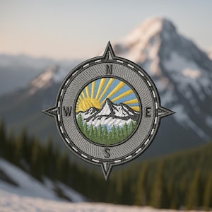May include: Embroidered patch featuring a compass design with a mountain and sun scene. The patch has a gray border with directional indicators and a detailed image of a mountain range, sun rays, and evergreen trees.