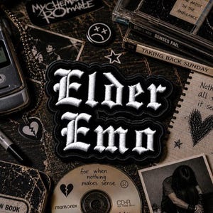 May include: A collection of emo-themed items, including a patch with the words "Elder Emo" in white lettering on a black background. Other items include CDs, a flip phone, a broken heart pendant, and handwritten notes.