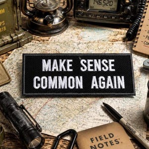 May include: A black rectangular patch with the words "MAKE SENSE COMMON AGAIN" in white block letters. The patch is surrounded by survivalist gear, including a radio, compass, flashlight, and a notebook with "FIELD NOTES" printed on it.