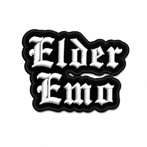 May include: A black and white embroidered patch with the words "Elder Emo" in a gothic font. The patch has a black border and is likely designed to be sewn onto clothing or accessories.