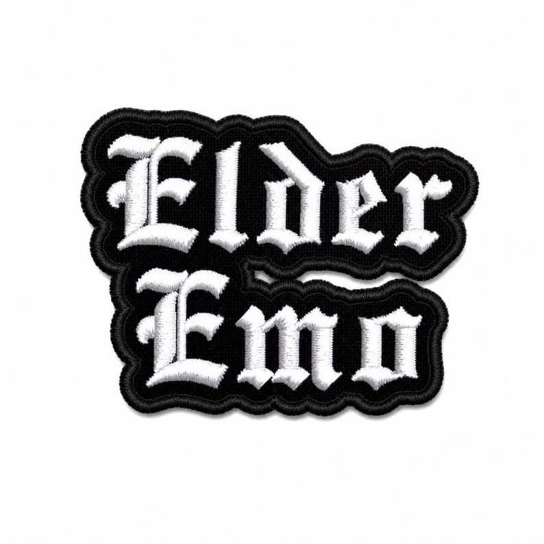 May include: A black and white embroidered patch with the words "Elder Emo" in a gothic font. The patch has a black border and is likely designed to be sewn onto clothing or accessories.