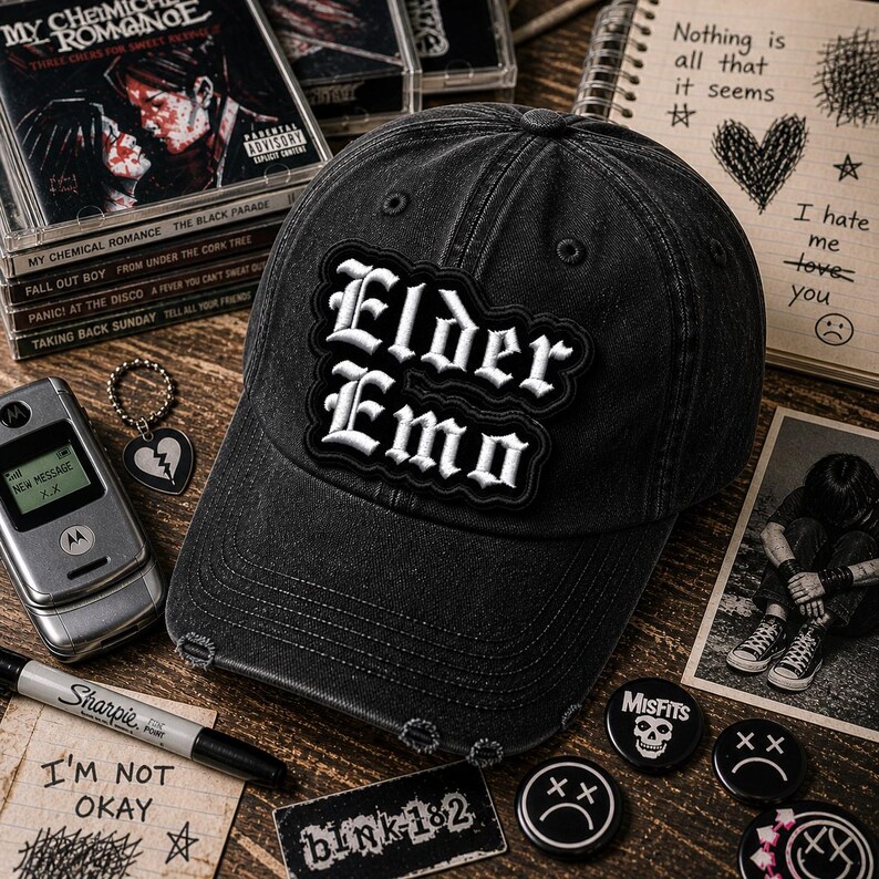 May include: Black denim baseball cap with the text "Elder Emo" in white lettering. The cap is distressed and surrounded by related accessories, including CDs, pins, and a flip phone.