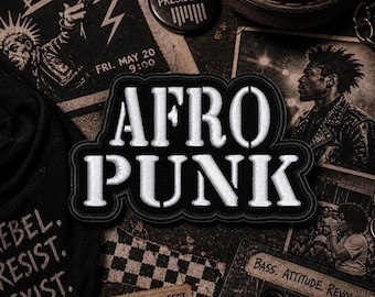May include: A black and white embroidered patch with the words "AFRO PUNK" in bold, white letters. The patch is surrounded by a black border. The image also includes a "DEAD PRESIDENTS" button and other punk-themed ephemera.