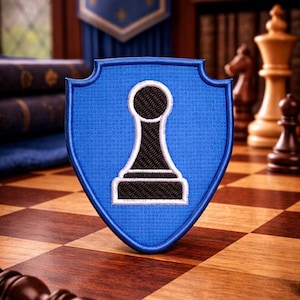 May include: A blue shield-shaped patch featuring a black and white chess pawn design with a white border. The patch is placed on a wooden chessboard, with other chess pieces and a banner in the background. The image evokes a classic board game.