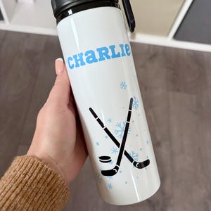 Gourde de hockey sur glace personnalisée avec votre nom, une image de hockey sur glace et un arrière-plan couleur flocon de neige. Cadeaux pour joueur de hockey sur glace.