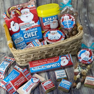 May include: A wicker basket filled with Christmas-themed gifts, including a jar of honey, a bag of nuts, a bag of sweets, and a box of cocoa mix. The gifts are wrapped in festive paper with Santa Claus illustrations and holiday greetings.