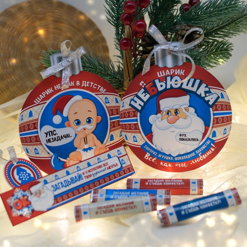 Puede incluir: Dos adornos navide&ntilde;os rojos y azules con un Pap&aacute; Noel y un beb&eacute;. Los adornos est&aacute;n decorados con copos de nieve blancos y un borde blanco. Los adornos est&aacute;n colgados de un &aacute;rbol de Navidad.