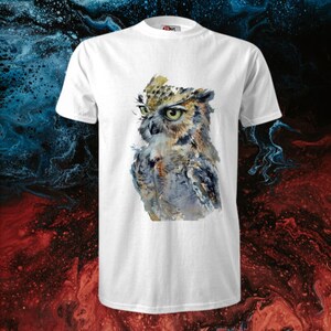 Op de afbeelding: Wit T-shirt met een aquarel-illustratie van een uil met bruine, grijze en witte veren. De uil kijkt naar links in de afbeelding.