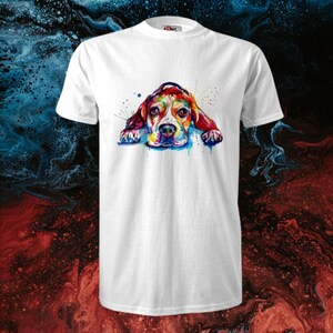 Op de afbeelding: Een wit T-shirt met een kleurrijke aquarel-illustratie van een beagle die ligt. De hond is geschilderd in tinten rood, oranje, geel, groen, blauw en paars.