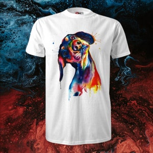 Op de afbeelding: Een wit T-shirt met een kleurrijk aquarel schilderij van een teckel. De hond kijkt omhoog en naar rechts, met zijn tong uitstekend. Het schilderij is gemaakt in tinten blauw, groen, geel, oranje, rood en paars.
