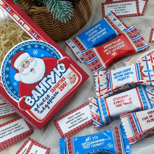 Puede incluir: Una caja roja y azul con una ilustraci&oacute;n de Pap&aacute; Noel y el texto "VANGUYO" y "Garant&iacute;a de felicidad - 200%". La caja est&aacute; llena de peque&ntilde;os caramelos envueltos con varios textos, incluyendo "Lee r&aacute;pido, luego comparte la alegr&iacute;a" y "&Aacute;brelo, te contar&eacute; algo".