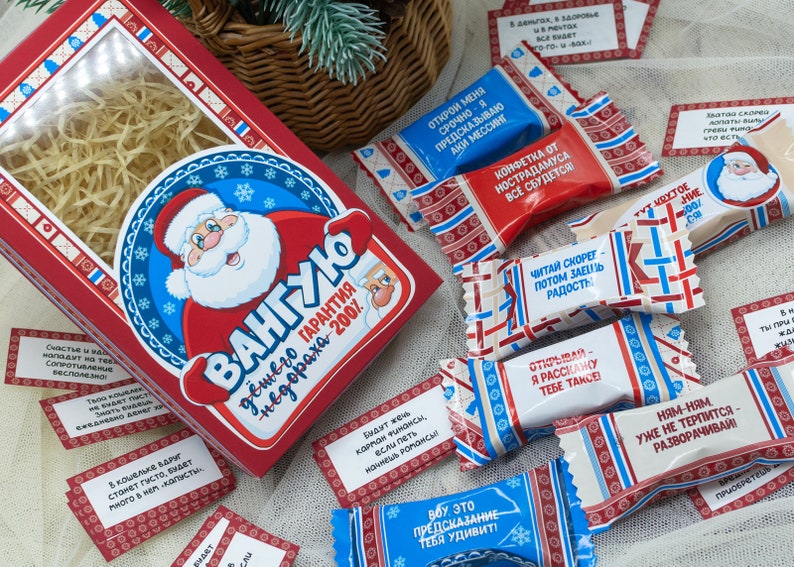 Puede incluir: Una caja roja y azul con una ilustraci&oacute;n de Pap&aacute; Noel y el texto "VANGUYO" y "Garant&iacute;a de felicidad - 200%". La caja est&aacute; llena de peque&ntilde;os caramelos envueltos con varios textos, incluyendo "Lee r&aacute;pido, luego comparte la alegr&iacute;a" y "&Aacute;brelo, te contar&eacute; algo".